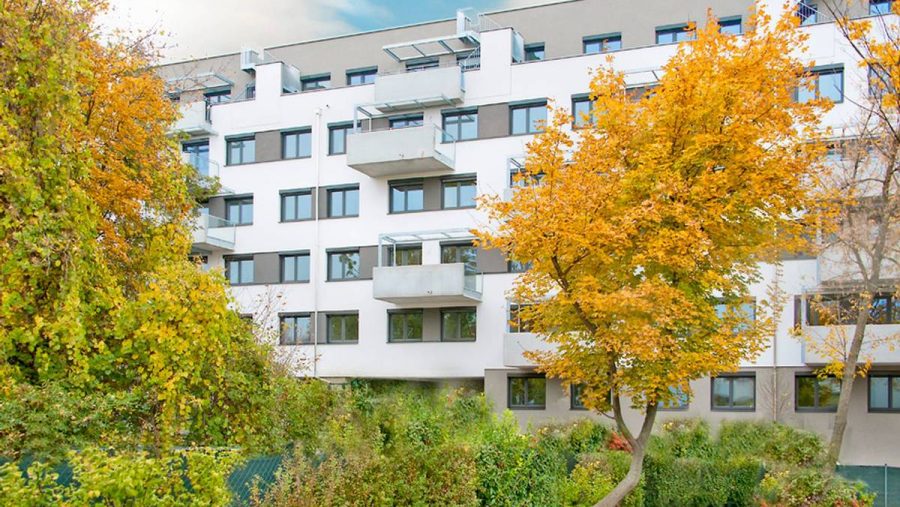 Mehrfamilienhaus im Herbst mit grünen Bäumen, Wohnung kaufen, moderne Architektur.