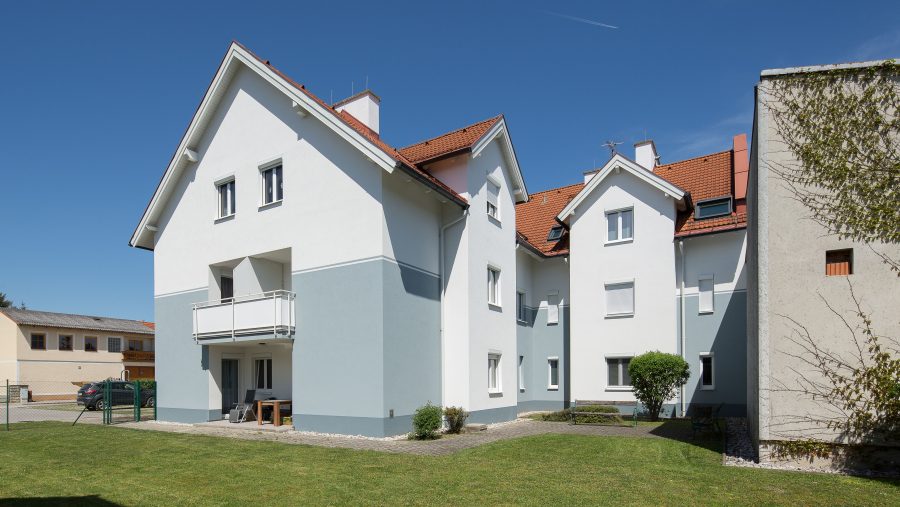 Weißes Wohnhaus mit rotem Dach und Garten bei klarem Himmel.