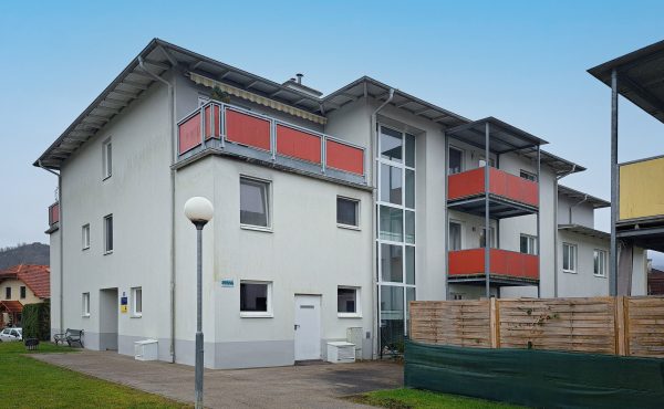 Mehrfamilienhaus mit roten Balkonen und gepflegtem Außenbereich an einem klaren Tag.