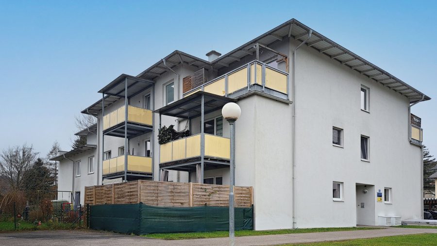 Mehrfamilienhaus mit Balkonen, modernes Design, blauer Himmel im Hintergrund.