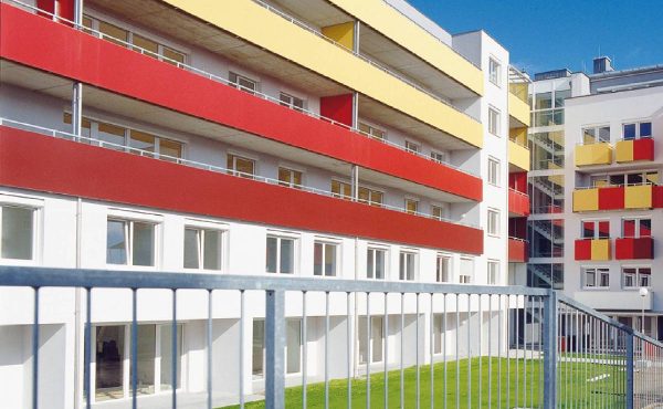 Modernes Gebäude mit farbigen Fassaden und Balkonen, blauer Himmel im Hintergrund.