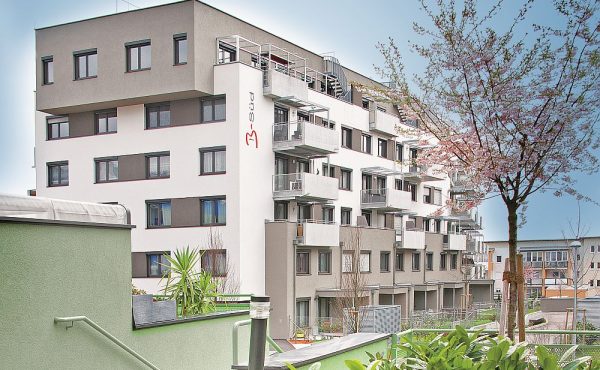 Mehrstöckiges Wohngebäude mit modernen Balkonen, umgeben von Bäumen und Pflanzen.