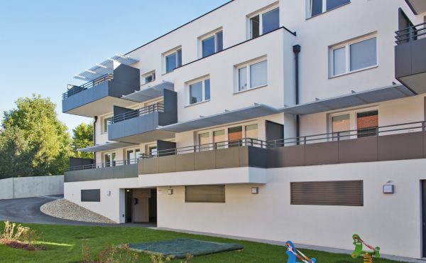 Moderne Wohnanlage bei Tageslicht, mit Balkonen und Grünflächen im Vordergrund.