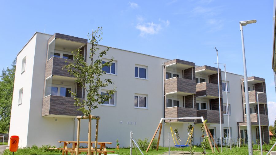 Mehrfamilienhaus mit Balkonen, umgeben von Grünfläche und Spielplatz bei klarem Himmel.