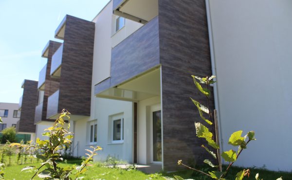 Moderne Wohngebäude mit Balkonen und Garten im Vordergrund bei sonnigem Wetter.