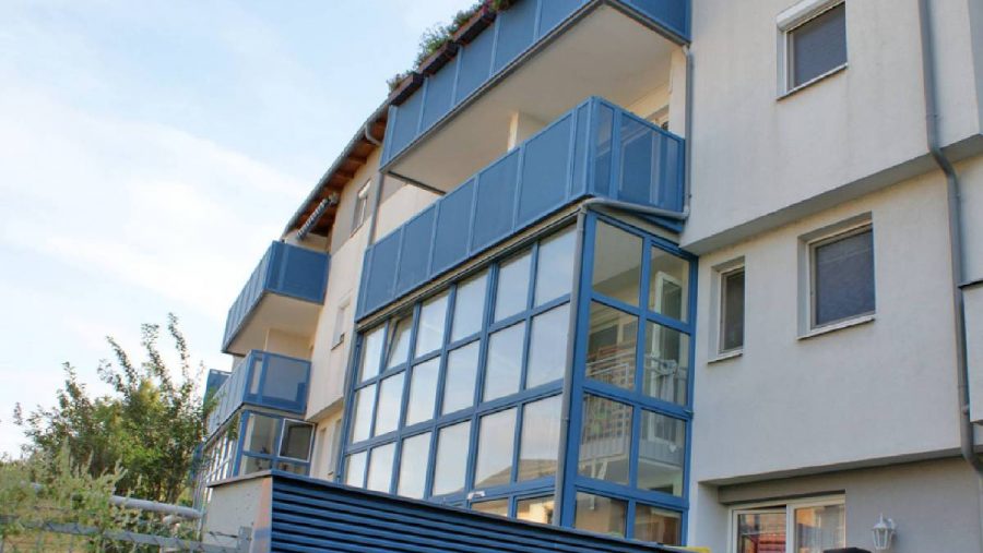 Mehrstöckiges Wohnhaus mit blauen Balkonen und großen Fenstern bei Tageslicht.