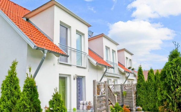 Reihenhäuser mit roten Dächern und Garten, blauer Himmel im Hintergrund.