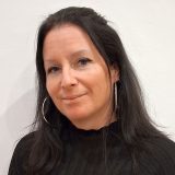 Porträt einer lächelnden Frau mit langen Haaren und großen Ohrringen.