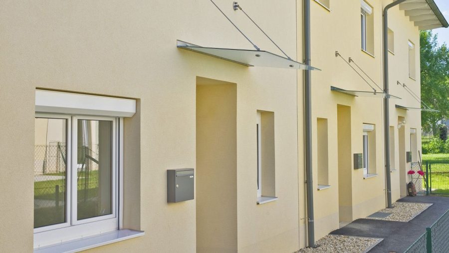 Reihenhausfassade mit Fenstern, Glasvordächern und Briefkästen in modernem Stil.